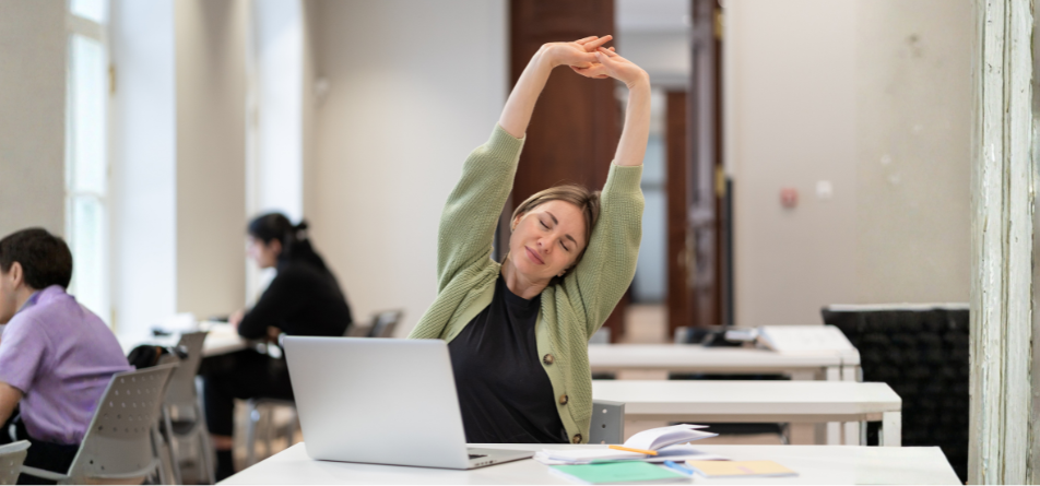 Frau am Schreibtisch führt eine Übung für Vielsitzer aus, indem sie den Oberkörper streckt 